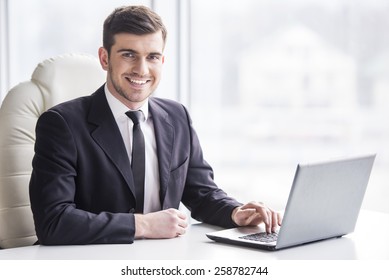 Handsome businessman is working with laptop in office is looking at the camera.