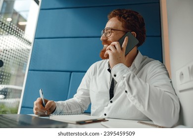 Handsome businessman working on project while using phone and making notes sittting in office - Shutterstock ID 2395459509