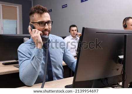 Handsome call center operator talking on phone and his colleagues working in modern office