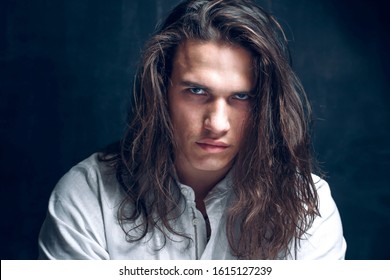 Handsome calm man. Portrait of a young muscular guy with long hair. Strong boy on an isolated dark background in the studio