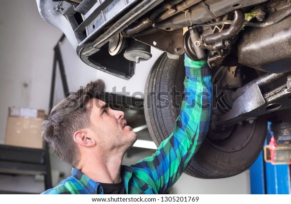 Handsome car mechanic checking\
suspension system of a lifted car at repair service station\
.