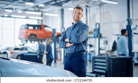 Handsome Car Mechanic is Posing in a Car Service. He Wears a Jeans Shirt and Safety Glasses. His Arms are Crossed. Specialist Looks at a Camera and Smiles. - Powered by Shutterstock