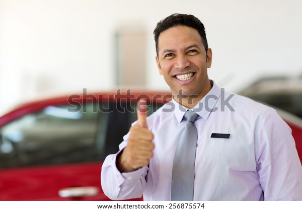 handsome car\
salesman thumb up at car\
dealership