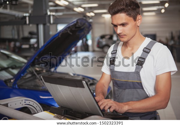 Handsome car technician doing\
computer diagnostics at the garade, repairing automobile, copy\
space. Attractive young auto mechanic working at car service\
station