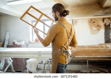Handsome carpenter checking the quality of the window frame before the paint at the carpentry workshop