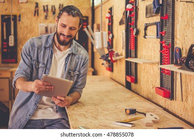 Handsome carpenter is using a digital tablet and smiling while working in the workshop - Powered by Shutterstock