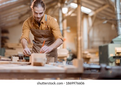 Handsome carpenter working with a wood, marking plank with a pencil in the carpentry workshop