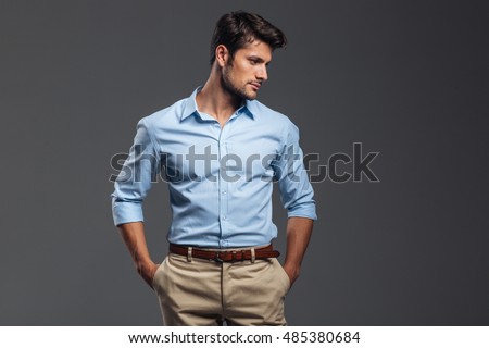 Handsome casual man standing with arms in pockets isolated on a gray background and looking away