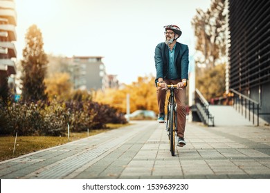 Un hombre de negocios casual de mediana edad está yendo a la oficina en bicicleta. Está conduciendo bicicleta delante del distrito de la oficina.