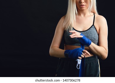 Handsome caucasian blonde Muay Thai fighter wrapping her hands with a band, preparing herself in boxing arena sport