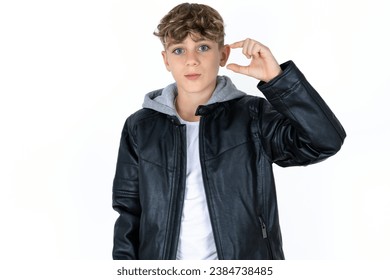 Handsome Caucasian boy  purses lip and gestures with hand, shows something very little.