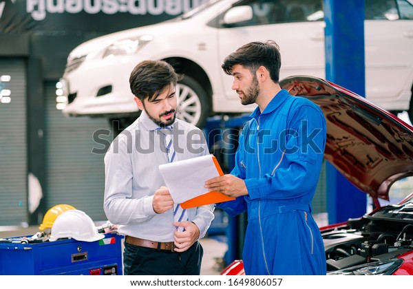 Handsome Caucasian businessman and auto service\
mechanic are discussing the work . Automotive mechanic pointing\
needed for the on automotive checklist document. Car repair and\
maintenance concept.