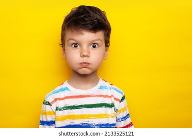 Handsome caucasian child wearing casual white T-shirt with bright stripes puffing cheeks with funny face. mouth inflated with air, crazy expression. High quality photo