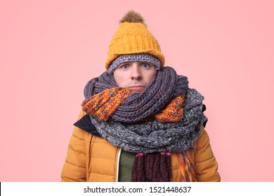 Handsome caucasian funny man in several hats and scarfs on pink background. Winter fashion.
