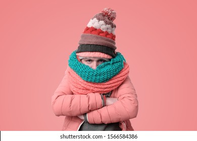 Handsome caucasian funny man in several hats and scarfs being offended or feeling cold on pink background. Winter fashion.