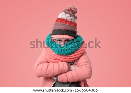 Handsome caucasian funny man in several hats and scarfs being offended or feeling cold on pink background. Winter fashion.