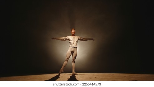 Handsome caucasian male ballet dancer performing pirouette and spinning on stage, wearing white tights, spotted by searchlight and isolated on black background  - Powered by Shutterstock