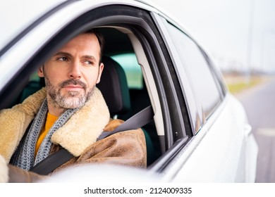 Handsome caucasian man with beard driving a car. Side window view. Driver on the road. 