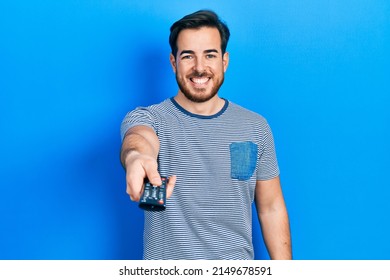 Handsome caucasian man with beard holding television remote control smiling and laughing hard out loud because funny crazy joke. 