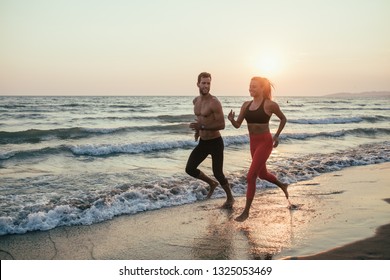 Handsome Caucasian man and beautiful woman running on sandy beach in sunset. - Powered by Shutterstock