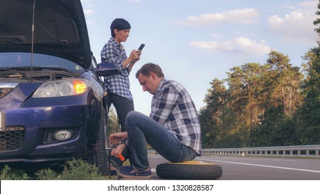 handsome caucasian man changing a tire on the side of the road. Woman using mobile phone messaging or scrolling social media on smartphone .