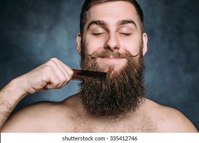 Handsome Caucasian Man With Funny Mustache And Closed Eyes Comb His Big Beard. Horizontal