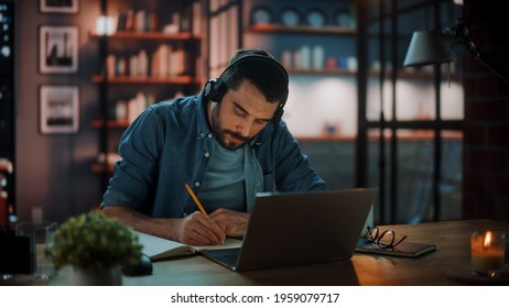 Handsome Caucasian Man With Headphones Listening Music on Laptop while Sitting in Dark Living Room in the Evening. Student Studying in Home School. Chat with Friends on Social Network. - Powered by Shutterstock