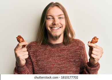 Handsome Caucasian Man With Long Hair Eating Chicken Wings Smiling With A Happy And Cool Smile On Face. Showing Teeth. 