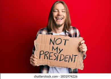 Handsome Caucasian Man With Long Hair Holding Not My President Protest Banner Smiling And Laughing Hard Out Loud Because Funny Crazy Joke. 