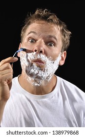 Handsome Caucasian Man With Messy Bed Head Hair Makes Funny Face While Shaving His Cheek On Black Background