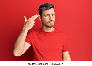 Handsome Caucasian Man Wearing Casual Red Tshirt Shooting And Killing Oneself Pointing Hand And Fingers To Head Like Gun, Suicide Gesture. 