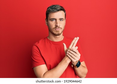 Handsome Caucasian Man Wearing Casual Red Tshirt Holding Symbolic Gun With Hand Gesture, Playing Killing Shooting Weapons, Angry Face 