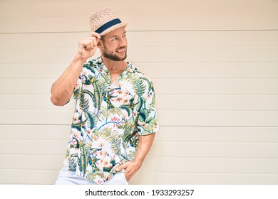 Handsome Caucasian Man Wearing Summer Hat And Flowers Shirt Smiling Happy Leaning On The Wall