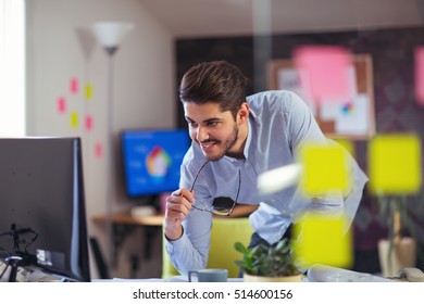 Handsome Caucasian man at work desk facing flat screen computer screen in office