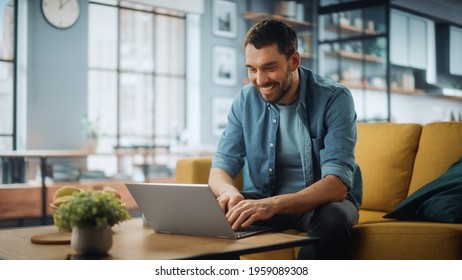 Handsome Caucasian Man Working on Laptop Computer while Sitting on a Sofa Couch in Stylish Cozy Living Room. Freelancer Working From Home. Browsing Internet, Using Social Networks, Having Fun.