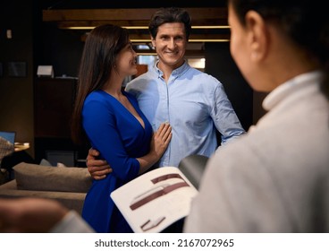 Handsome Caucasian Mature Man Hugging His Wife, Smiling While Talking To Sales Rep While Looking For New Upholstered Furniture In Home Design Studio. Business, Consumerism, Commerce, Human Relations