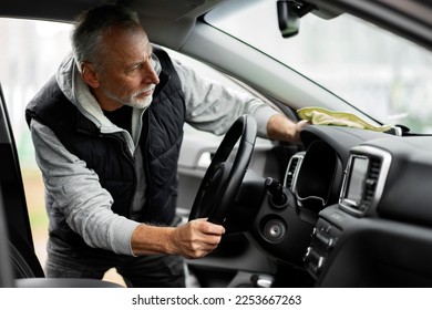 Handsome Caucasian senior active male driver, cleaning his car at self service car wash. He's wiping interior, steering wheel and dashboard with yellow microfiber cloth, waxing and polishing scratches - Powered by Shutterstock