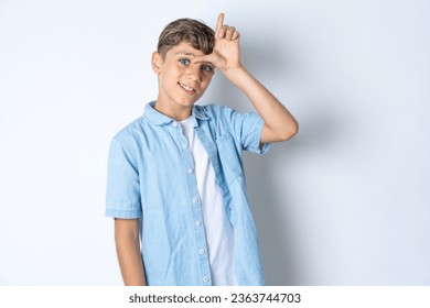 Handsome Caucasian teenager boy wearing denim jacket making fun of people with fingers on forehead doing loser gesture mocking and insulting. - Powered by Shutterstock