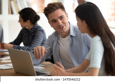 Handsome caucasian young guy helping asian female groupmate with abstract or sharing ideas about new school project. Mixed race happy students working together on homework, collaborating in classroom. - Powered by Shutterstock