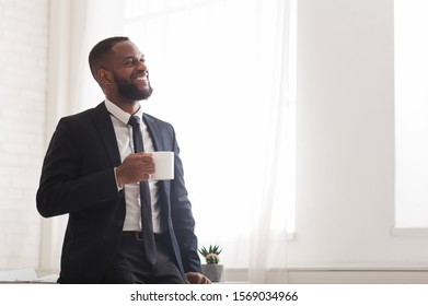 Handsome Cheerful African American Businessman Drinking Coffee Near Window In Office Excited After Successful Deal, Copy Space