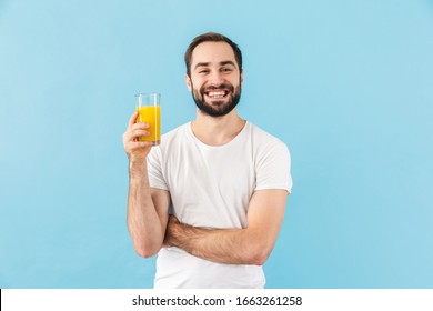 Handsome cheerful young bearded man wearing t-shirt standing isolated over blue background, showing glass of fresh orange juice - Powered by Shutterstock