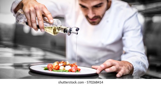 Handsome chef pouring olive oil on meal in a commercial kitchen - Shutterstock ID 570268414