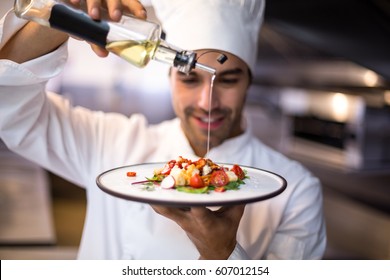 Handsome chef pouring olive oil on meal in a commercial kitchen - Shutterstock ID 607012154