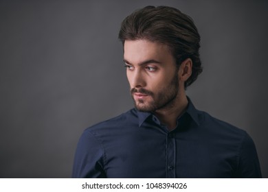 Handsome Confident Businessman With Bristle, In Dark Blue Shirt Is Looking Away, On Gray Background