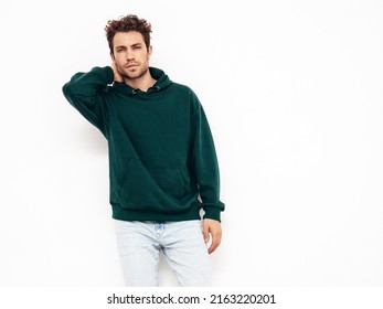 Handsome confident hipster  model.Sexy unshaven man dressed in summer stylish green hoodie and jeans clothes. Fashion male with curly hairstyle posing in studio. Isolated on white