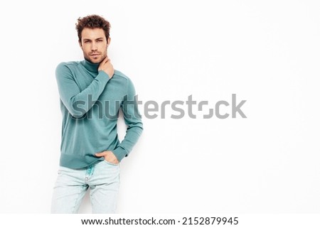 Handsome confident hipster  model.Sexy unshaven man dressed in summer stylish blue sweater and jeans clothes. Fashion male with curly hairstyle posing in studio. Isolated on white