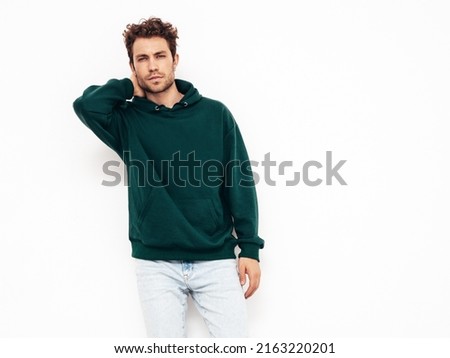 Handsome confident hipster  model.Sexy unshaven man dressed in summer stylish green hoodie and jeans clothes. Fashion male with curly hairstyle posing in studio. Isolated on white