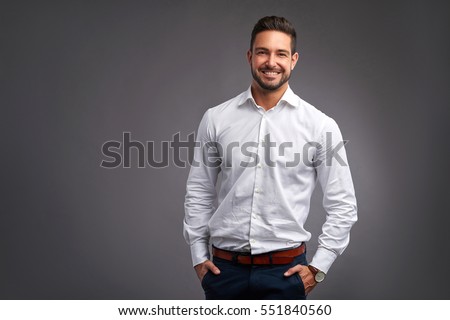 A handsome confident young man standing and smiling in a white shirt.