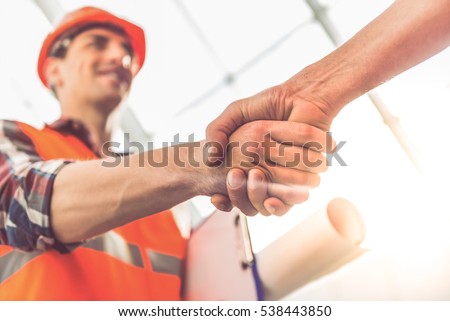 Handsome construction workers in protective helmets and vests are shaking hands while working in the office center