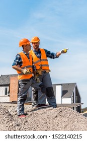 Handsome Constructor Pointing With Finger While Standing On Stones Near Coworker 